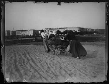Ohne Titel (Zwei Frauen ziehen und schieben gemeinsam den Handkarren durch den Sand, Blick auf die Knobelsdorffbrücke)