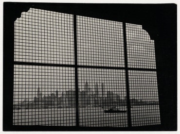 Blick durch vergitterte Fenster des Internierungsgebäudes von Ellis Island auf die Wolkenkratzer von New York